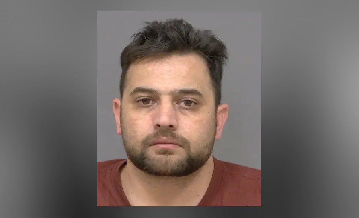 Close-up of a man with short dark hair and a trimmed beard, looking straight at the camera with a neutral expression against a plain background.