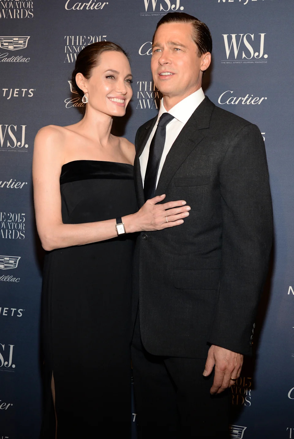 A couple poses on the red carpet at an awards event. The woman wears an elegant strapless gown, and the man is in a classic dark suit and tie