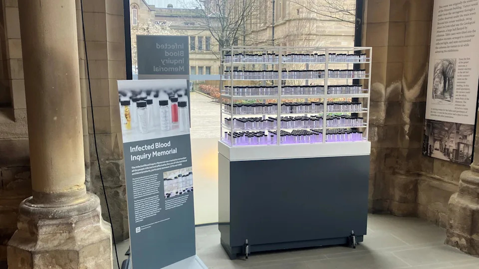 Photograph of the memorial to the victims of the NHS blood infection scandal. The image shows a display case, with blood vials containing personal messages from those affected.