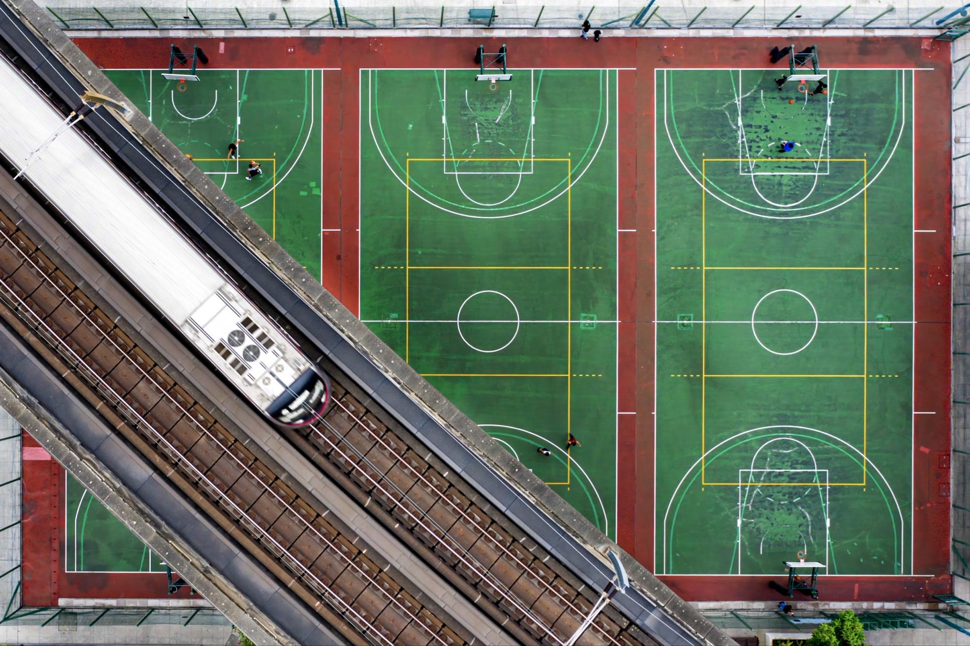 An aerial photo of three basketball courts with a train going over the top of them