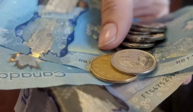 A person holding Canadian bills and coins in an outstretched hand.