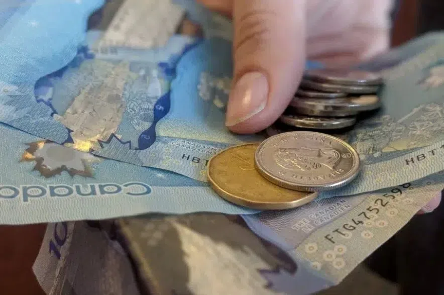 A person holding Canadian bills and coins in an outstretched hand.