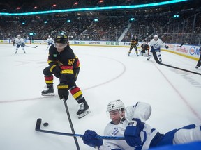 Vancouver Canucks' Teddy Blueger and Tampa Bay Lightning's Brayden Point vie for the puck along the boards.