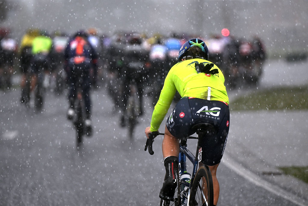 A rider in bright yellow shown in the view from behind the peloton as heavy rain falls