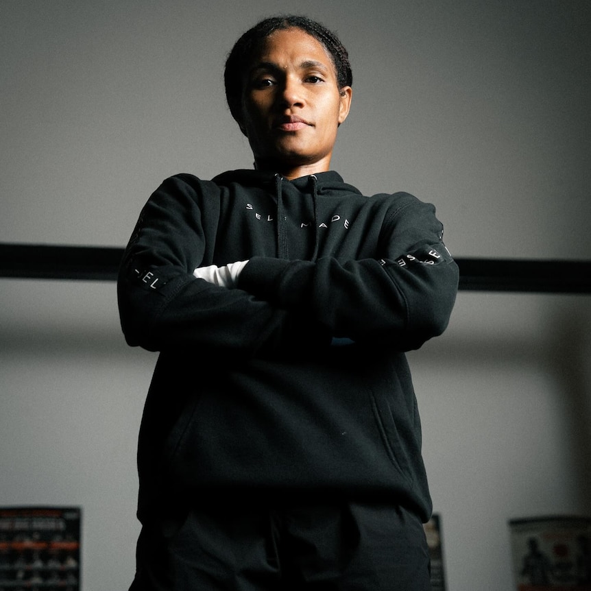 A young Papua New Guinean woman stands in a boxing pose with arms raised in fists wearing a black sports bra 