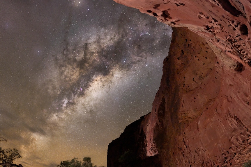 The Milky Way set against a reddish orange rock wall.