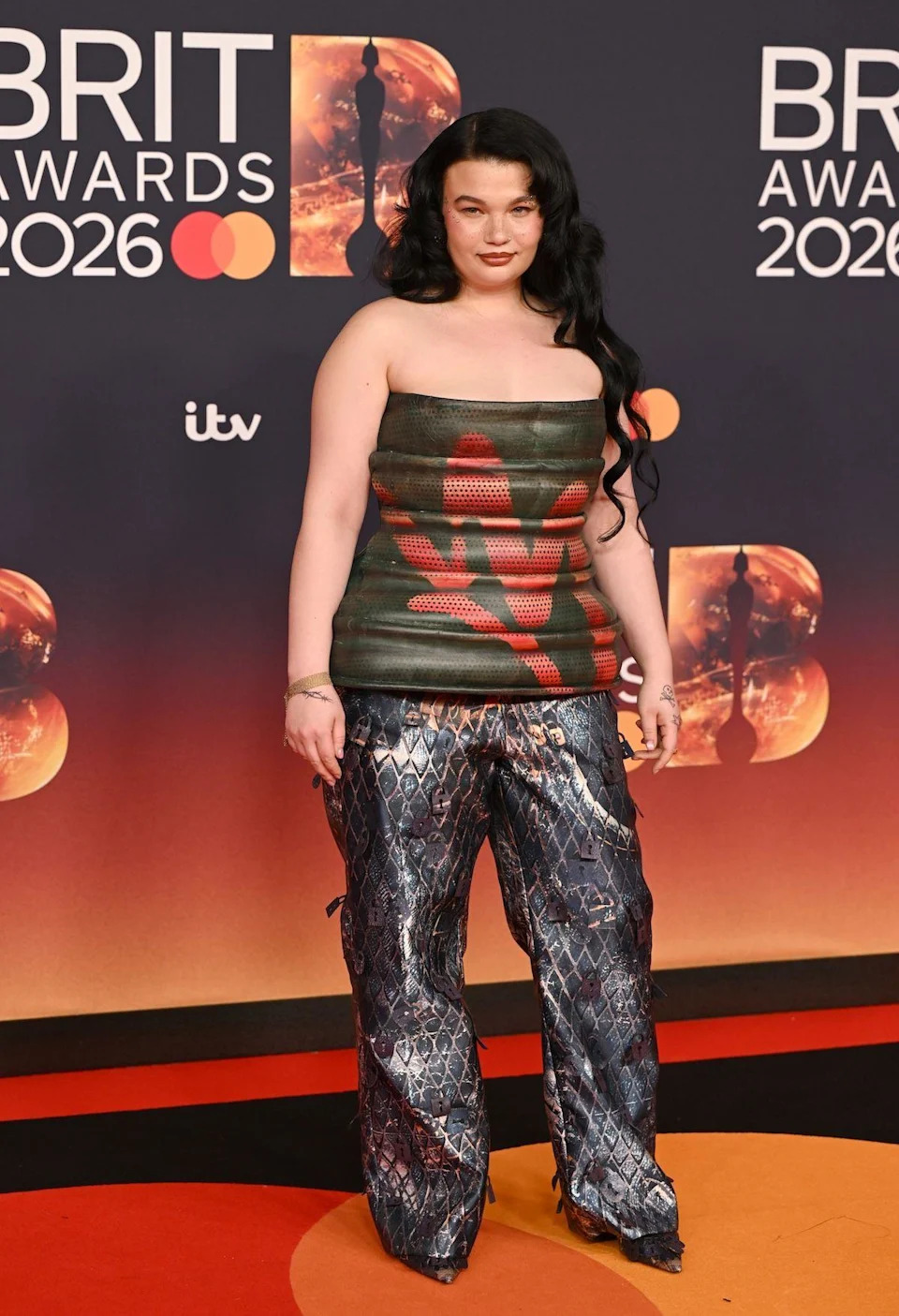 Lola Young in a green leather peplum top and snake trousers