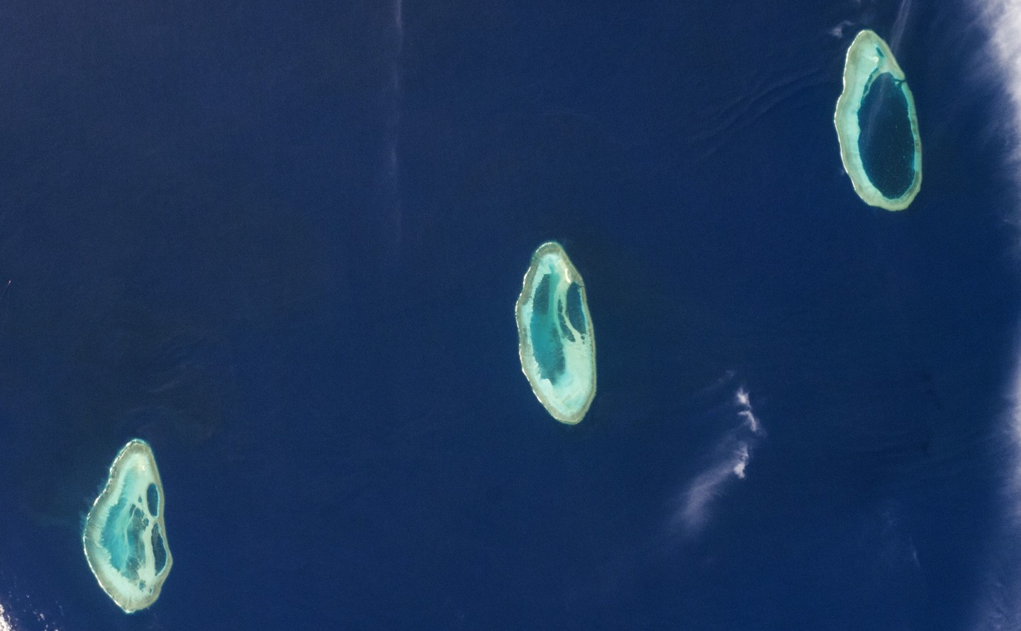 Satellite photo of three oval-shaped atolls in a straight line in the ocean