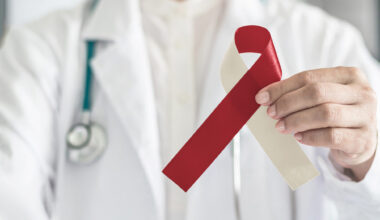 Burgundy ivory ribbon awareness on doctor's hand, symbolic bow color for head and neck cancer, oral squamous cell carcinoma, throat, laryngeal and pharyngeal cancer. (iStock)