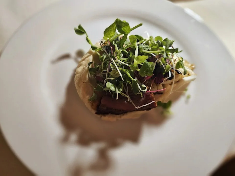 Sliced pork belly over braised cabbage, topped with a tangle of microgreens.