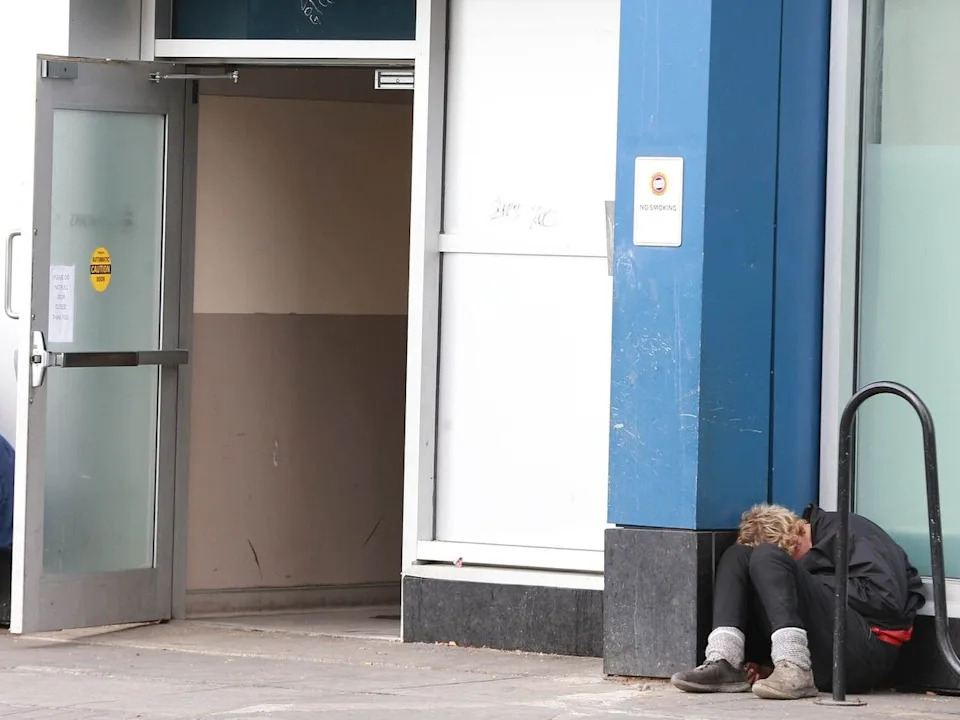  A man is huddled against a pillar outside the supervised drug consumption site at the Sheldon M. Chumir Health Centre on October 29, 2024.