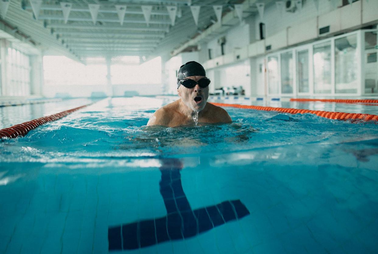 Active senior man swimmer swimming in indoors swimming pool.