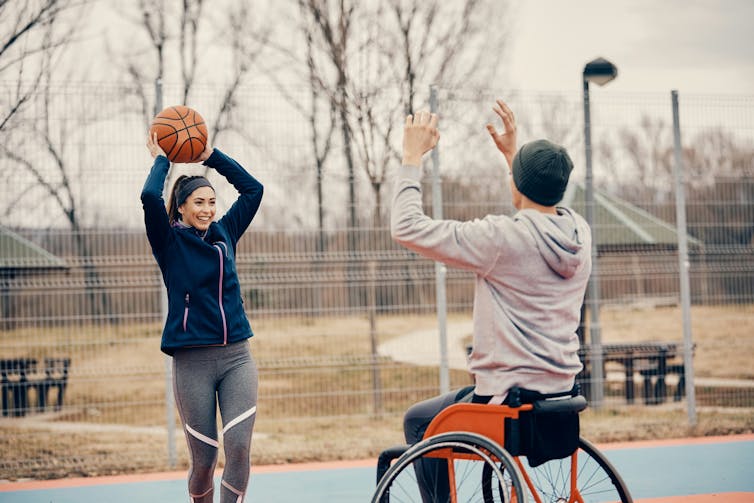 Woman throws basketball to a man in a wheelchair.