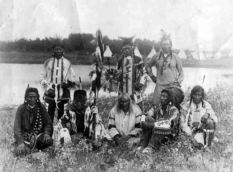 A historical photoraph of a group of Cree men standing and sitting next to each other.
