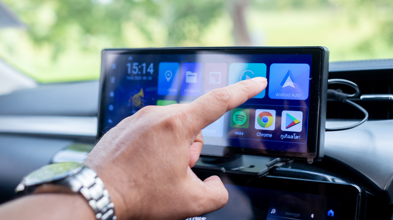 A hand reaching for the Android Auto icon on a car's infotainment display