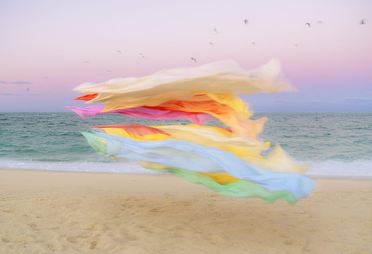 A photograph by Thomas Jackson of numerous pieces of colorful fabric that are seemingly suspended in the air on a beach