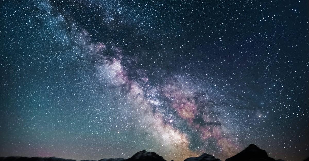 Stars and the Milky Way hang over black mountain tops