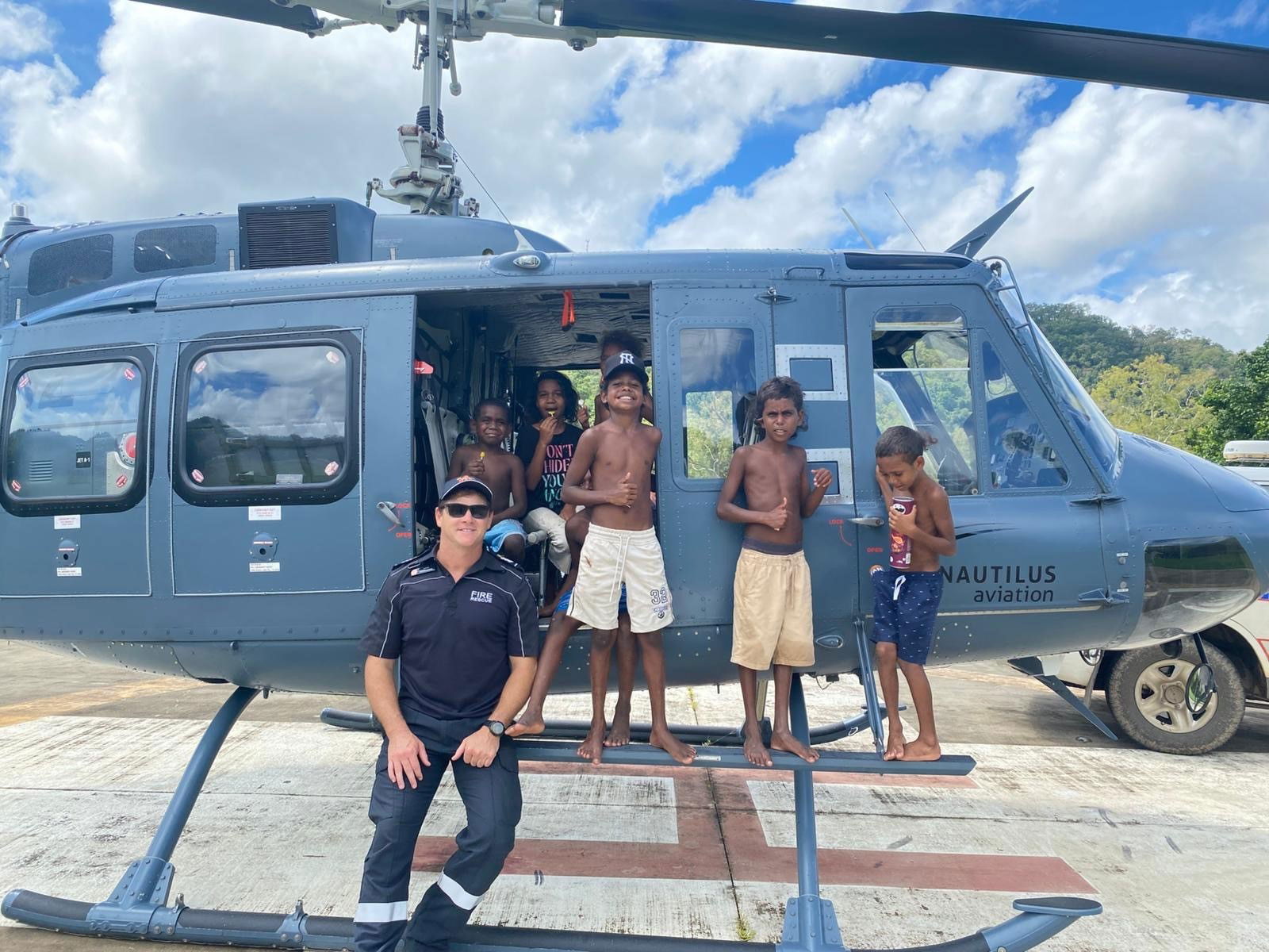A man sits on the side of a helicopter with kids beside him. 