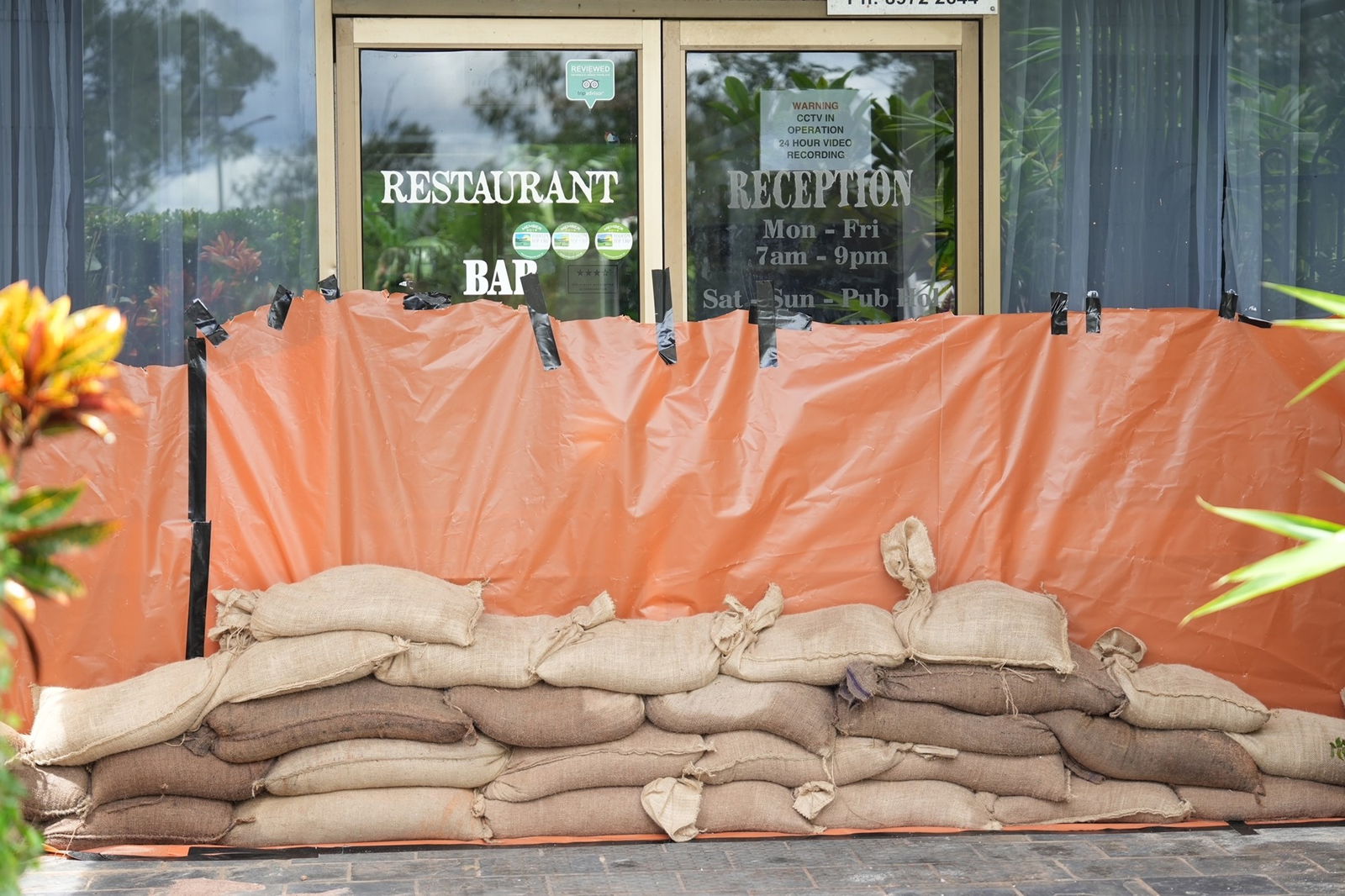 Orange tarpe surrounding the front entrance of a resturant, with sandbags piled in front of it.