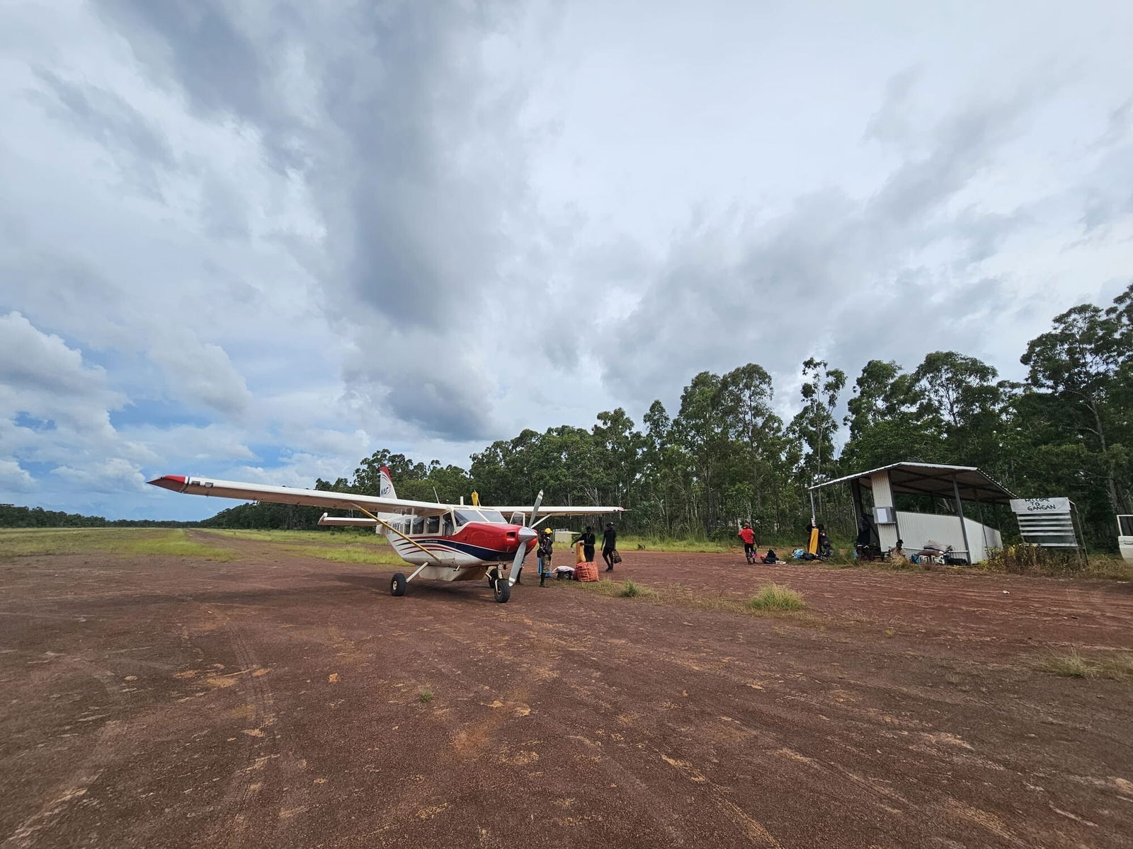 A small plane, a grouple of five people standing near it as they load goods into it.