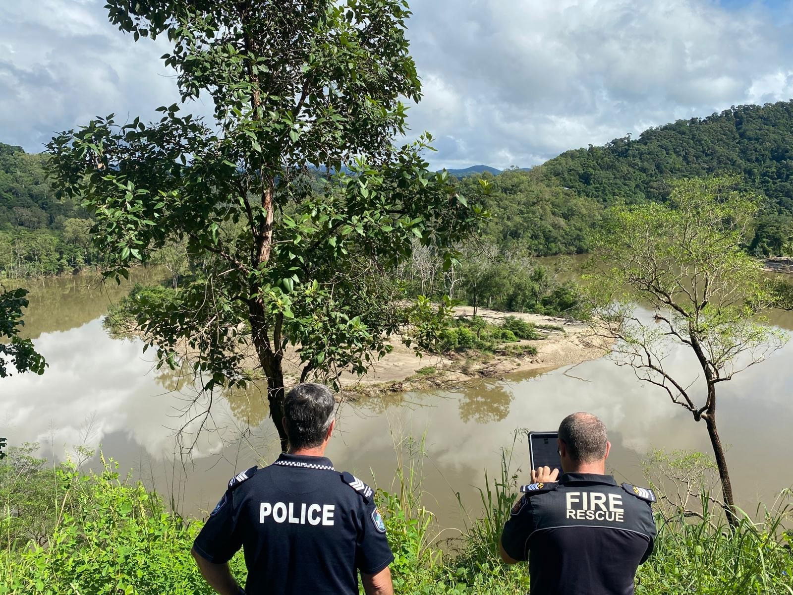 Two police officers look at a flooded area of vegetation. 