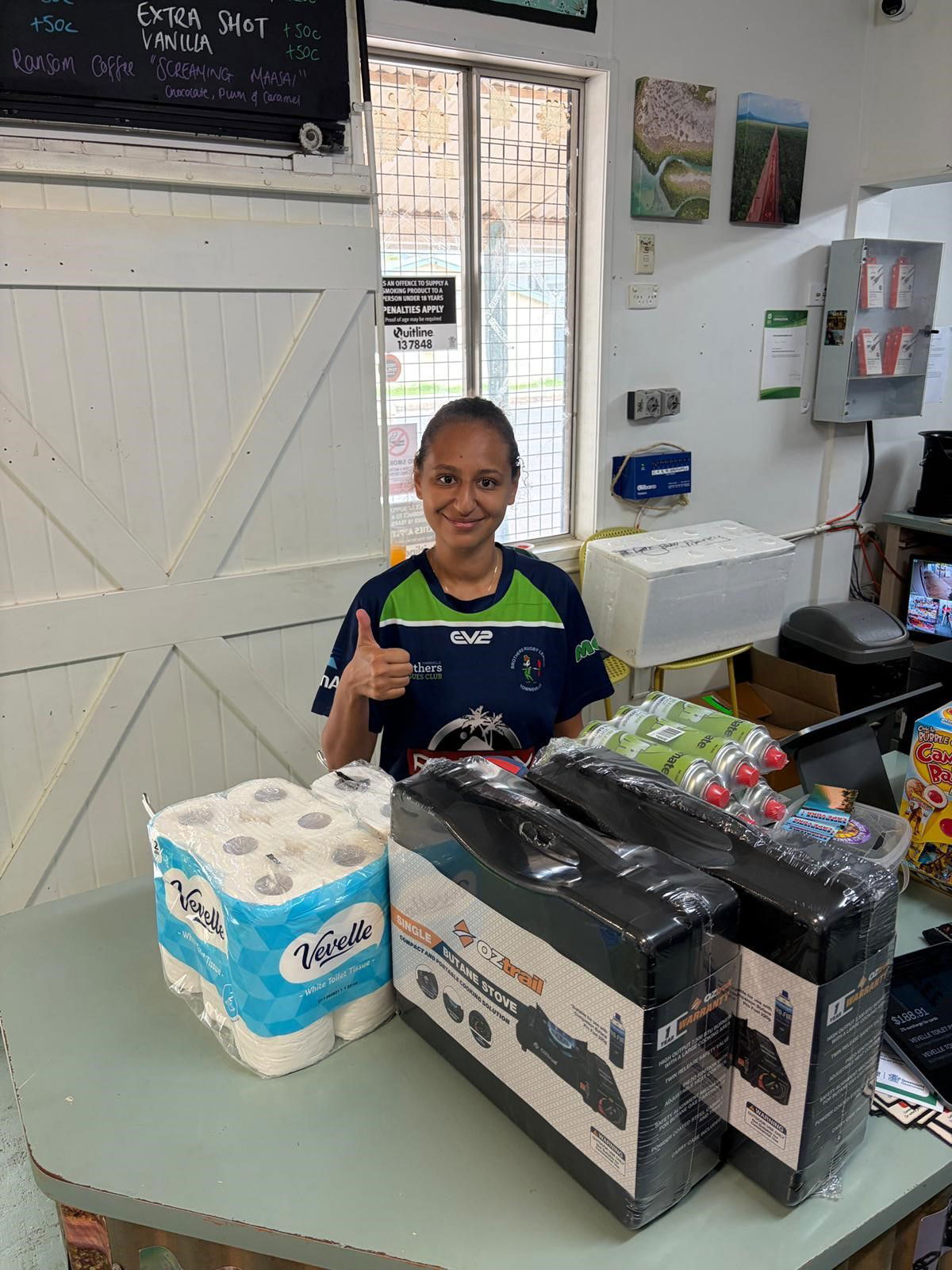 A woman giving a thumbs up behind the counter of a small grocery store