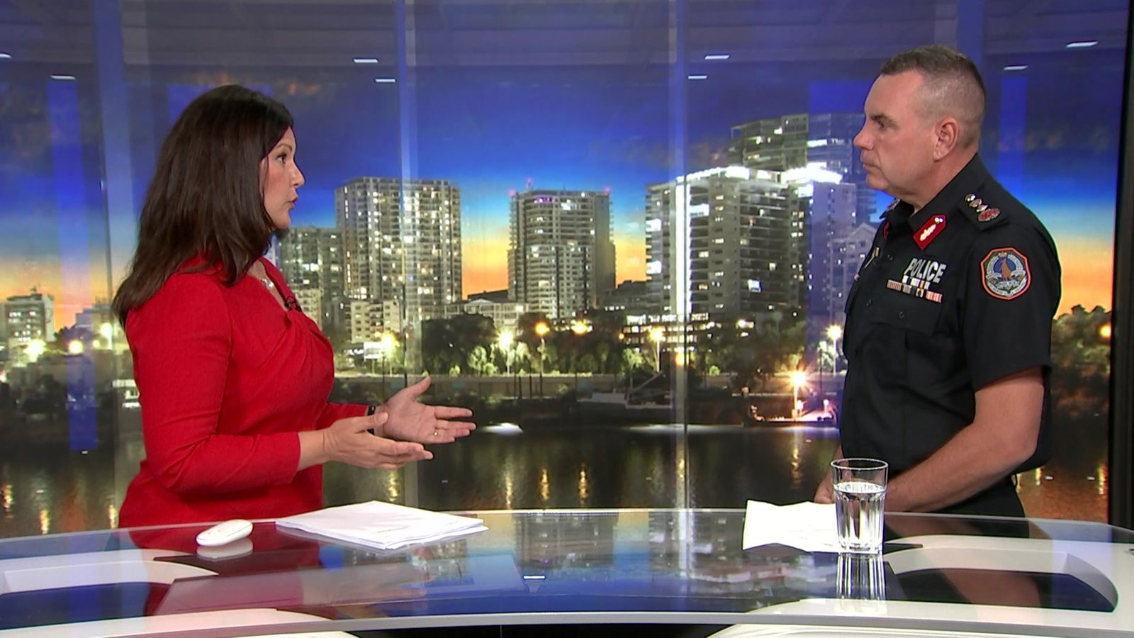 A woman and a man in a police uniform talking inside a TV news studio.