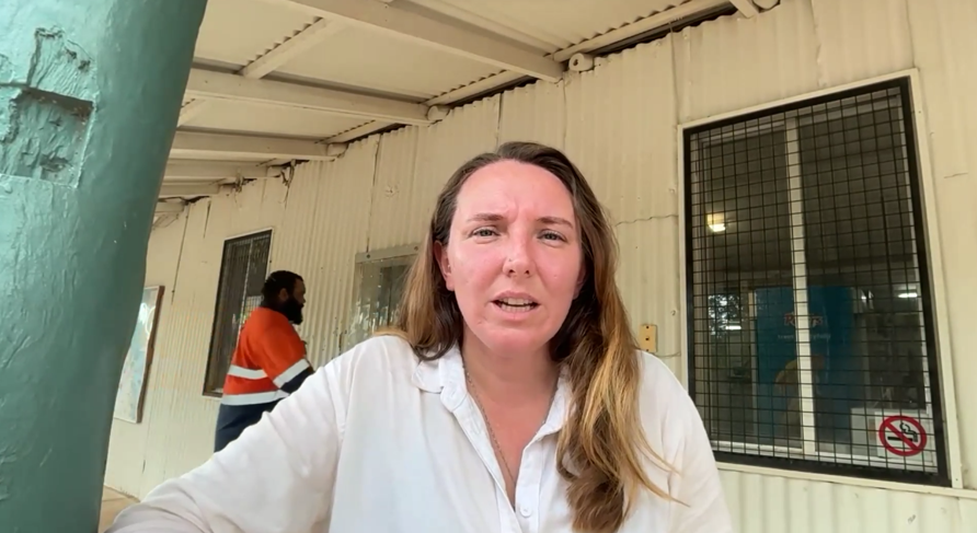 A woman outside a corrugated iron building 