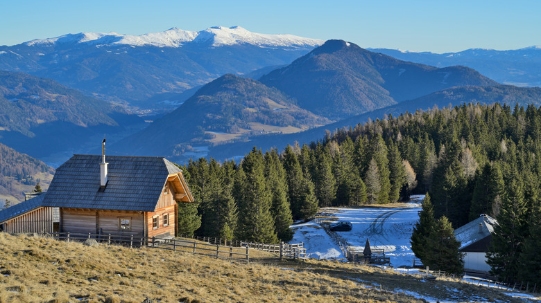 wooden cabin on a slope with snow clad mountains in the background