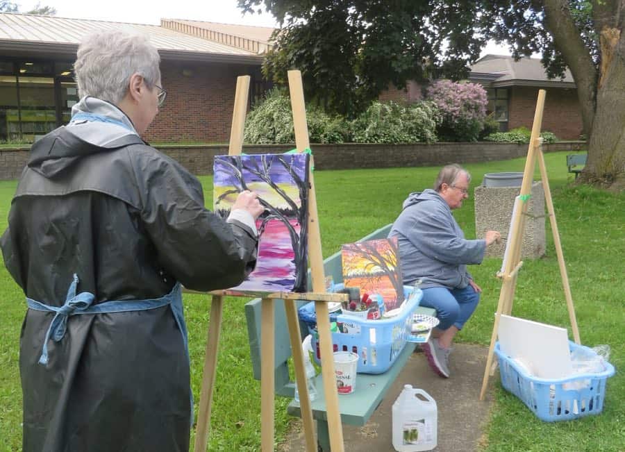 two women standing at easels outdoors painting nature scenes in one of paint with janet's art classes near Ottawa