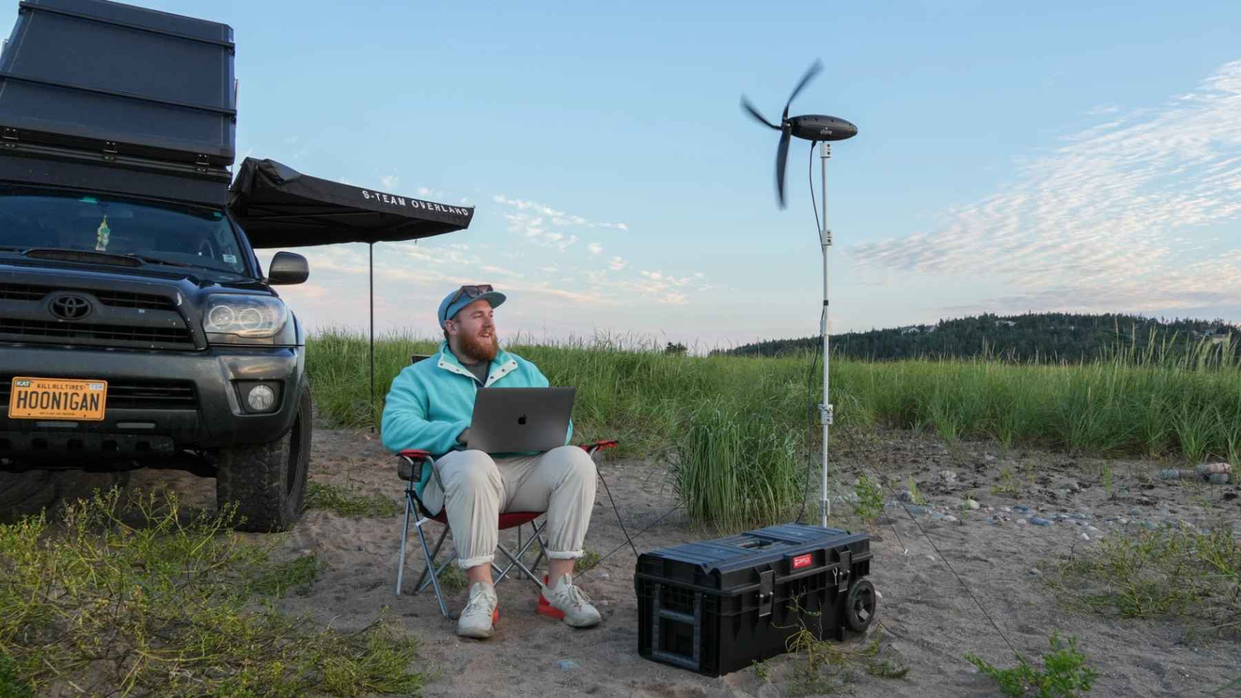 Portable wind turbine generating electricity while a camper works on a laptop during an off grid camping trip