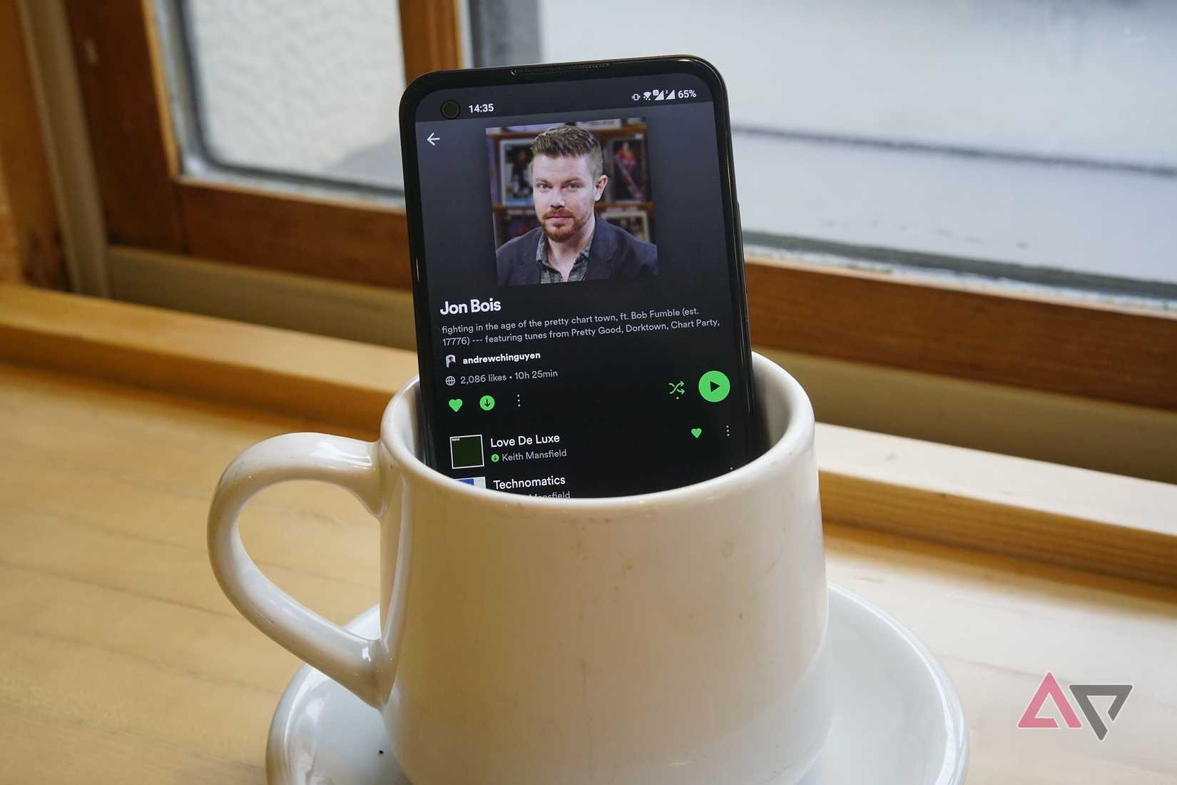 spotify on the scren of a phone that is stiting in a coffee cup