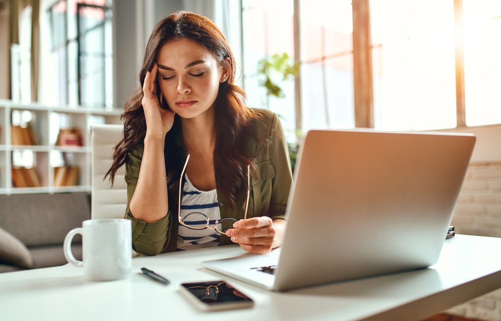 A young woman experiencing a migraine attack while working on a laptop at home.