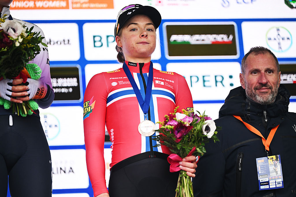 Norwegian champion Mie Bj&oslash;rndal Ottestad stands on the podium of Trofeo Alfredo Binda 2026 after finishing third, wearing a medal and holding a bouquet of flowers