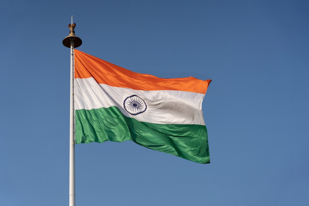 The Indian national flag waves from a flagpole against a blue sky.
