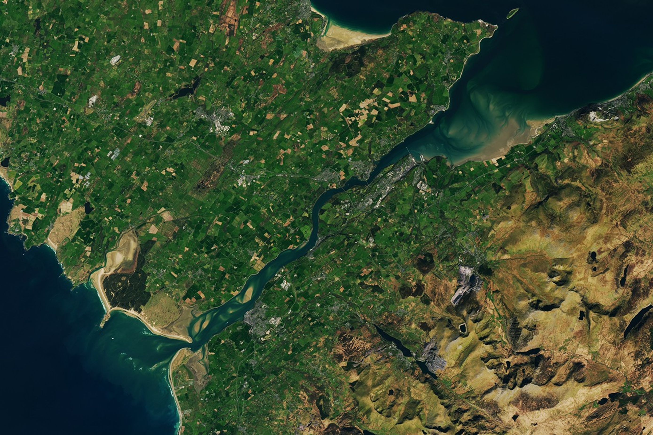 A wider view of the same area shows how the Strait of Menai connects to the open ocean to the north and south of Anglesey island. The right side of the image transitions to hillier terrain with less farmland.