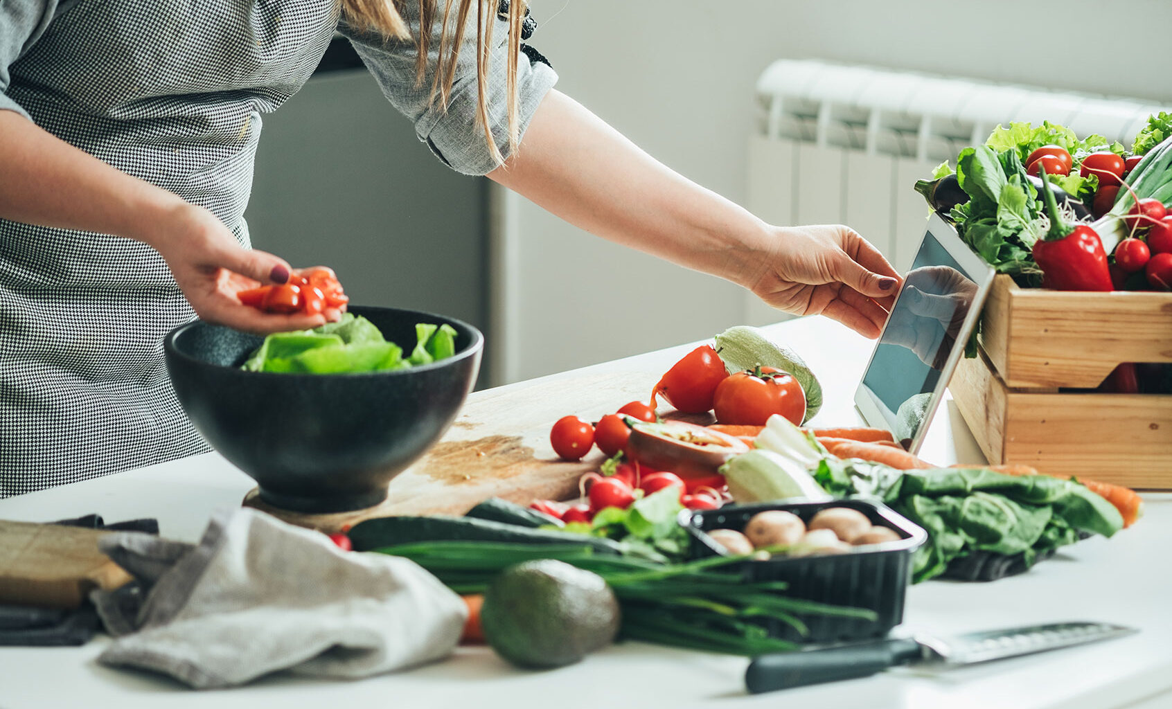 Woman utilizing tablet in the kitchen while cooking (Getty Images/Tijana Simic)