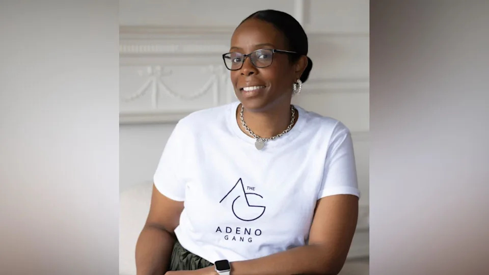 Tanya Simon-Hall is smiling at the camera, and is wearing a white branded t-shirt which read 'Adeno Gang'