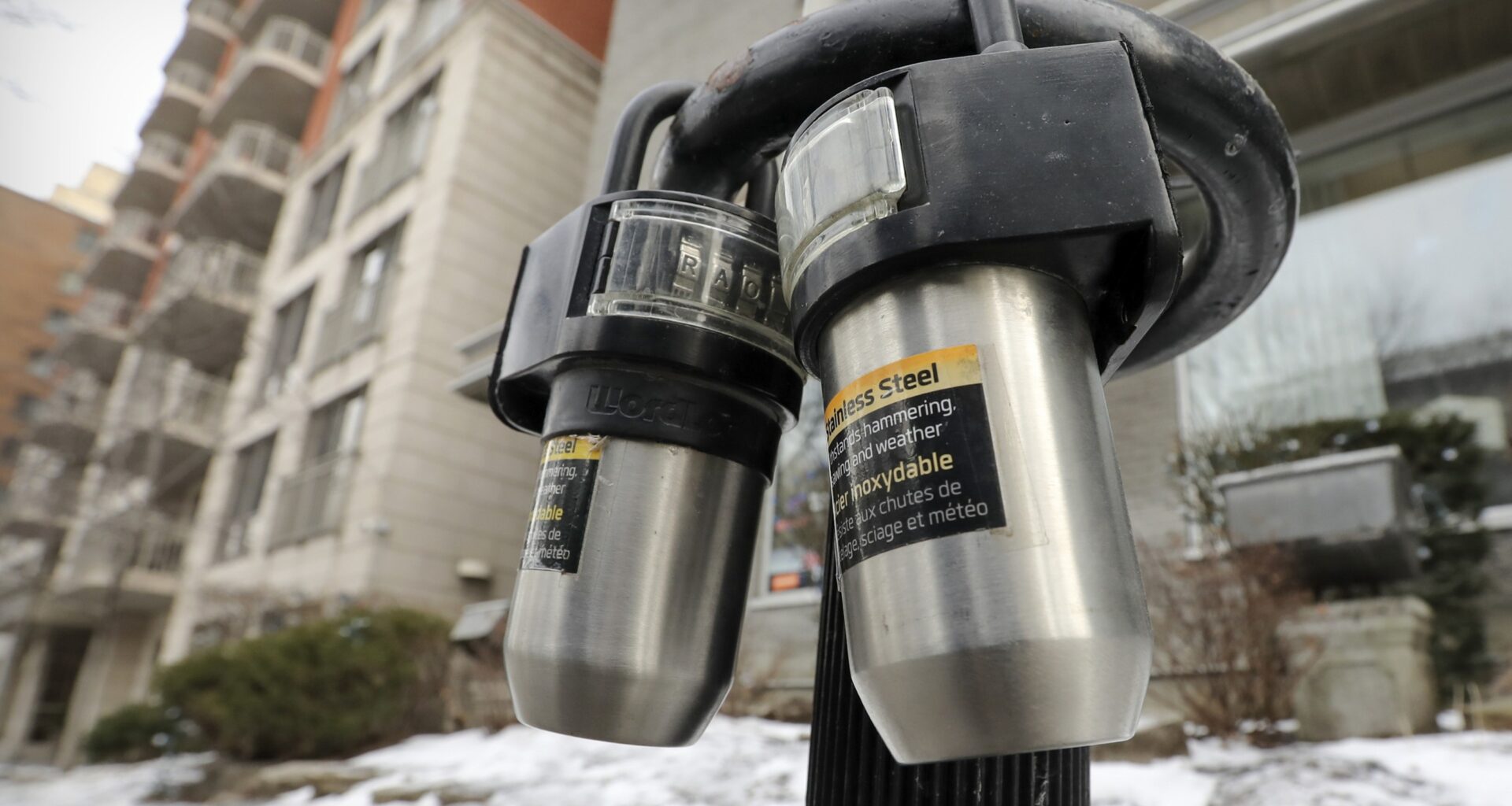 Lock boxes hung on a parking meter and bicycle parking ring outside an apartment building.