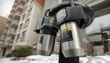 Lock boxes hung on a parking meter and bicycle parking ring outside an apartment building.