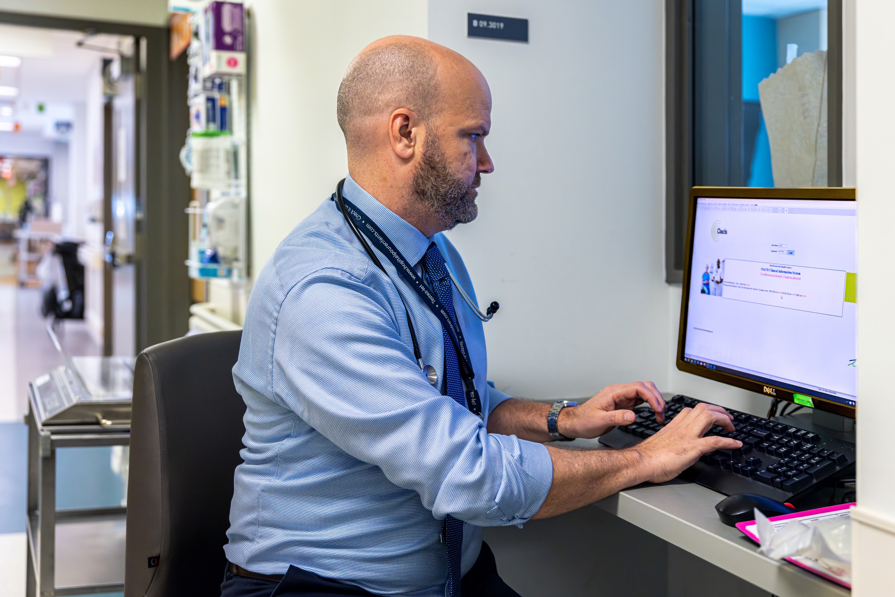 A doctor works on a computer in an alcove of a hospital.
