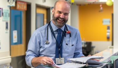 A doctor laughs while looking up from a medical file in the hallway of a hospital.