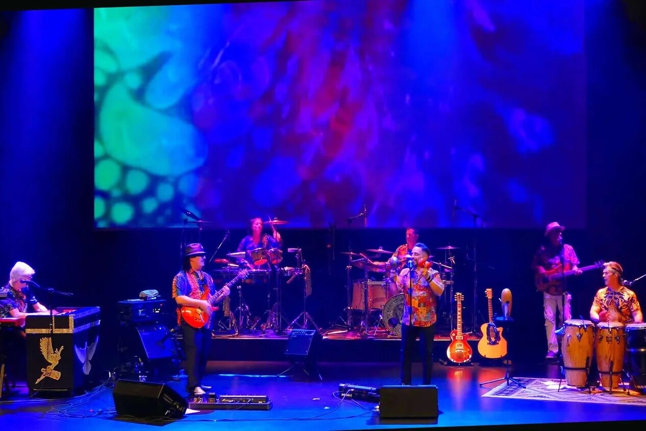 A band performs on stage in blue light in front of a psychedelic backdrop.