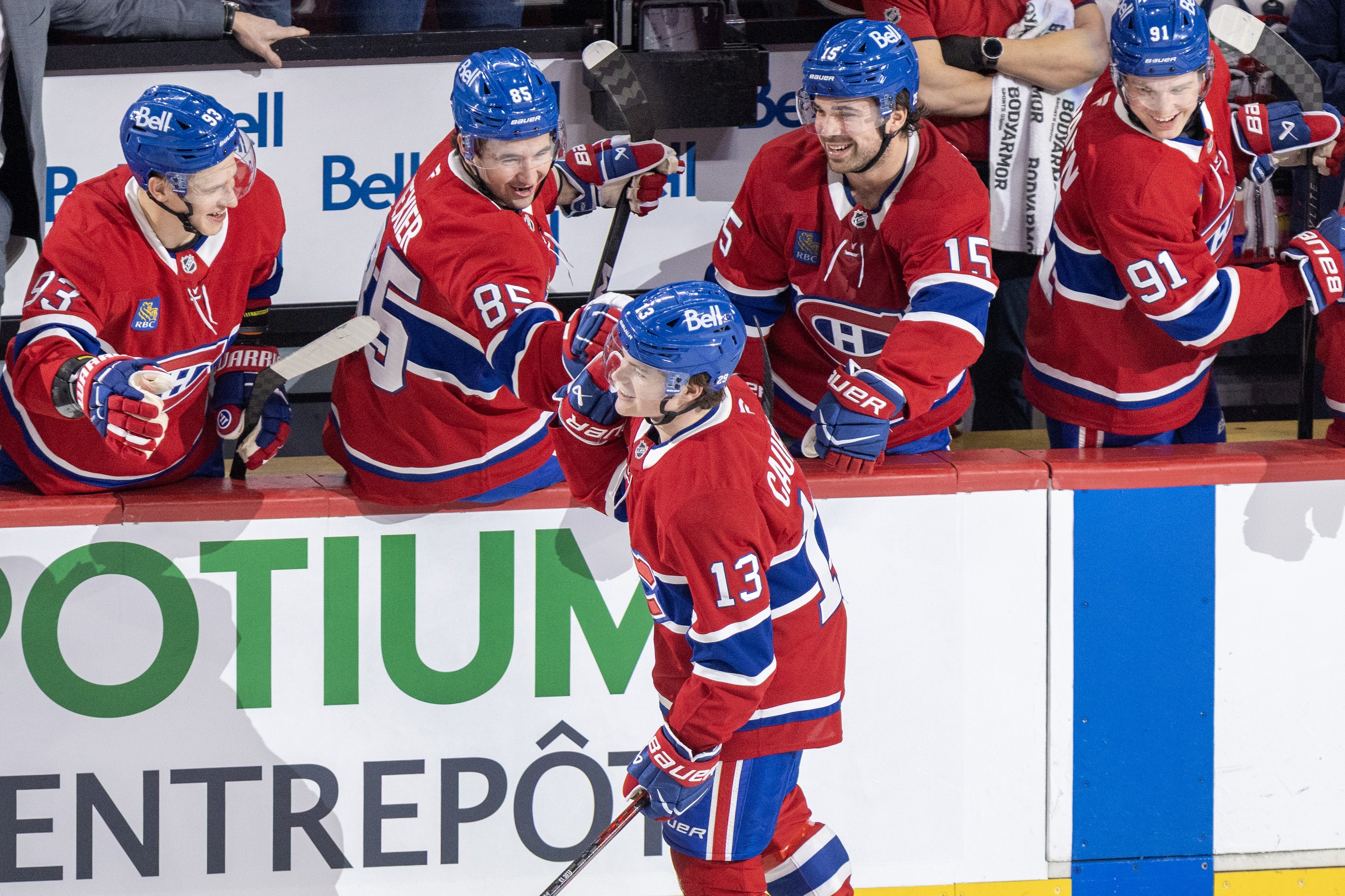 Hockey players on the bench congratulate a teammate skating by after he scored a goal.