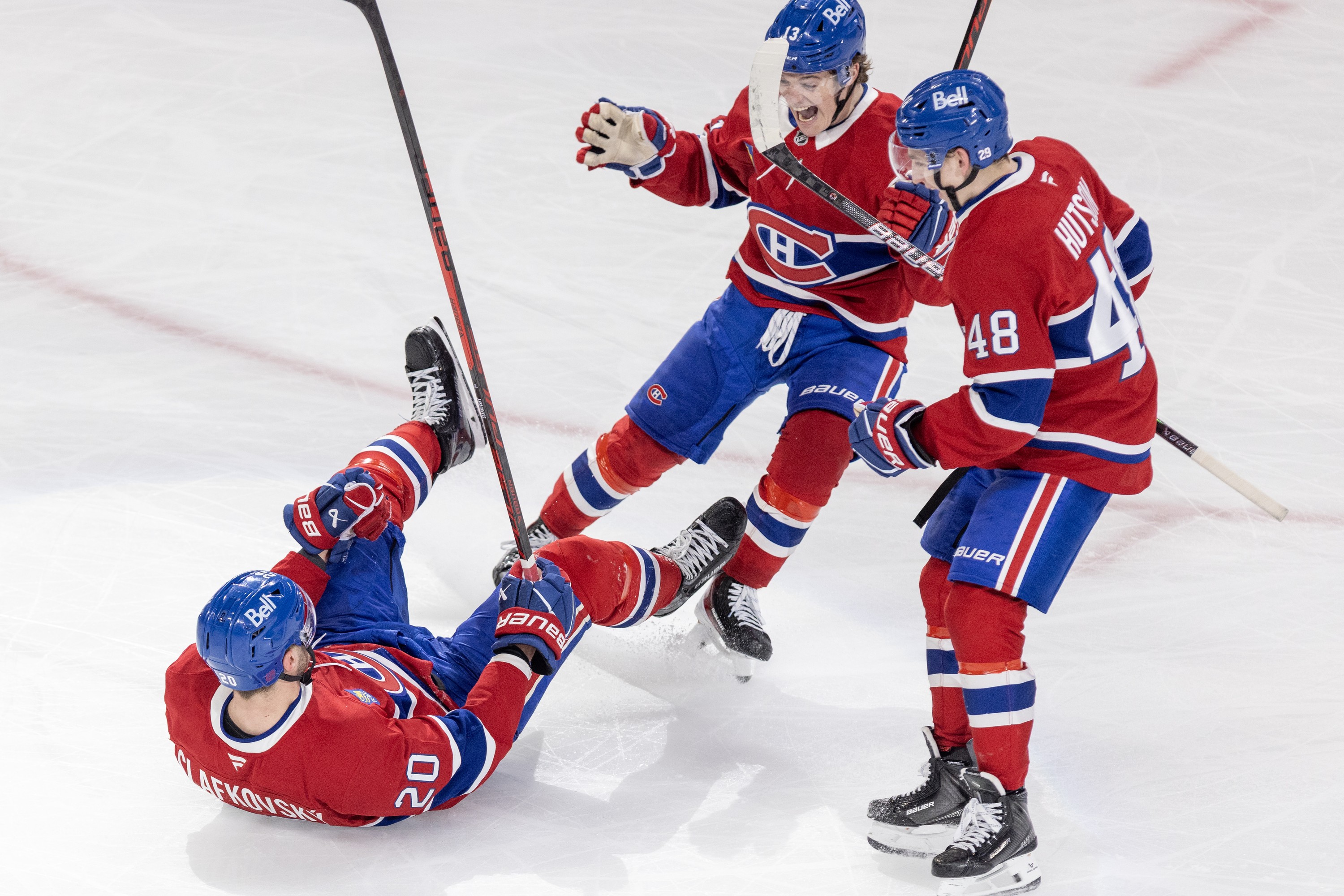 Hockey player is on his back on the ice to celebrate winning a game with two teammates standing over him. 