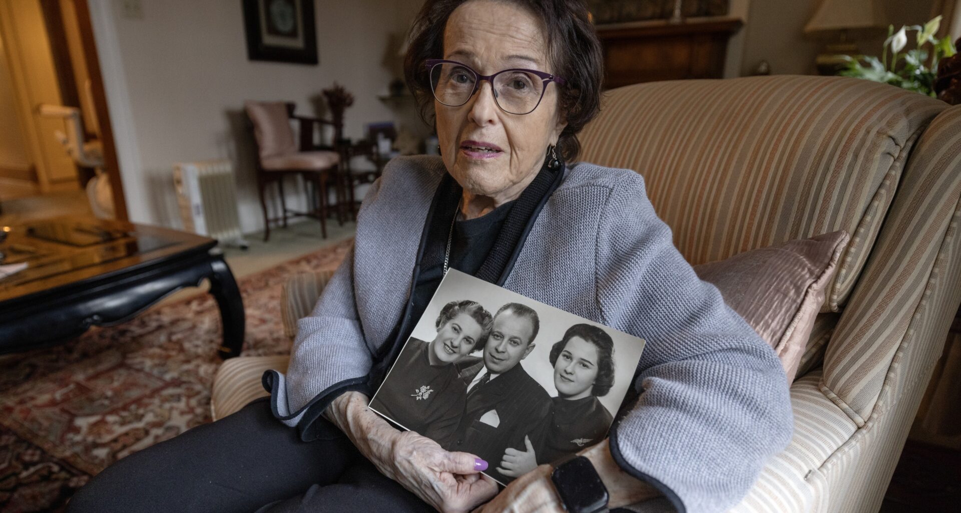 A woman holds a black and white family photo of her and her parents from the 1950s in her living room.