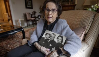 A woman holds a black and white family photo of her and her parents from the 1950s in her living room.