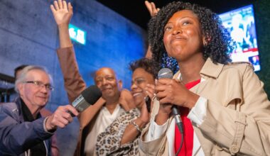 Tatiana Auguste clutches a handheld microphone as she stands in a crowded room.