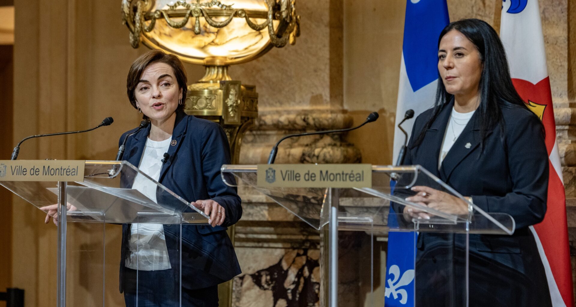 Two women stand at podiums addressing the media