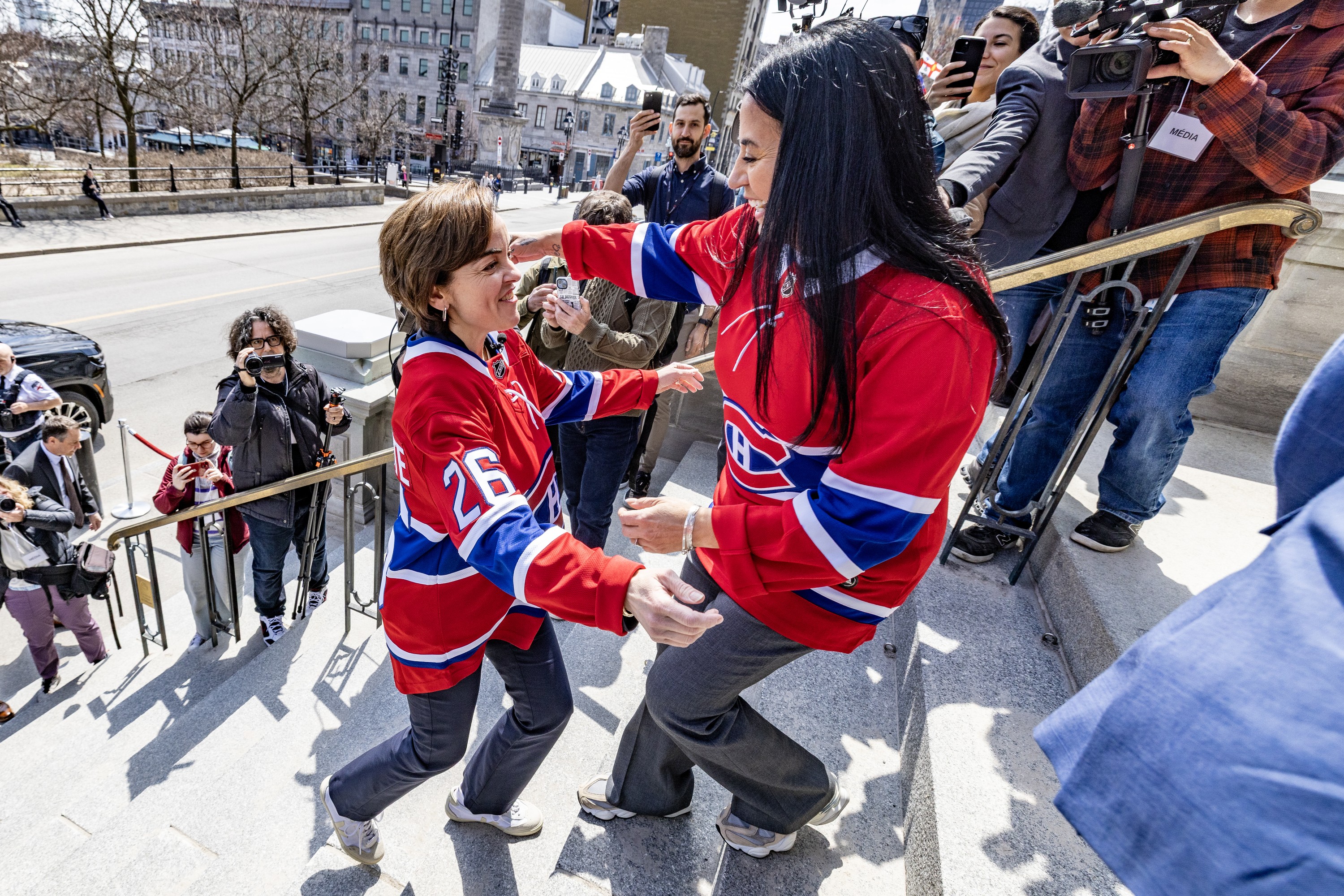 Two women wearing Habs jerseys meet on steps of city hall.